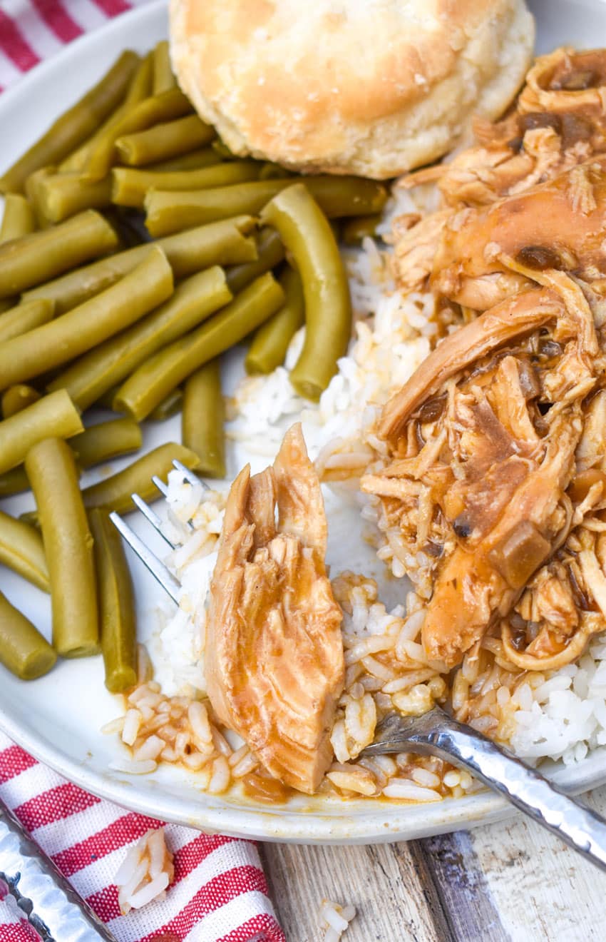 crockpot chicken and gravy over steamed white rice on a white dinner plate