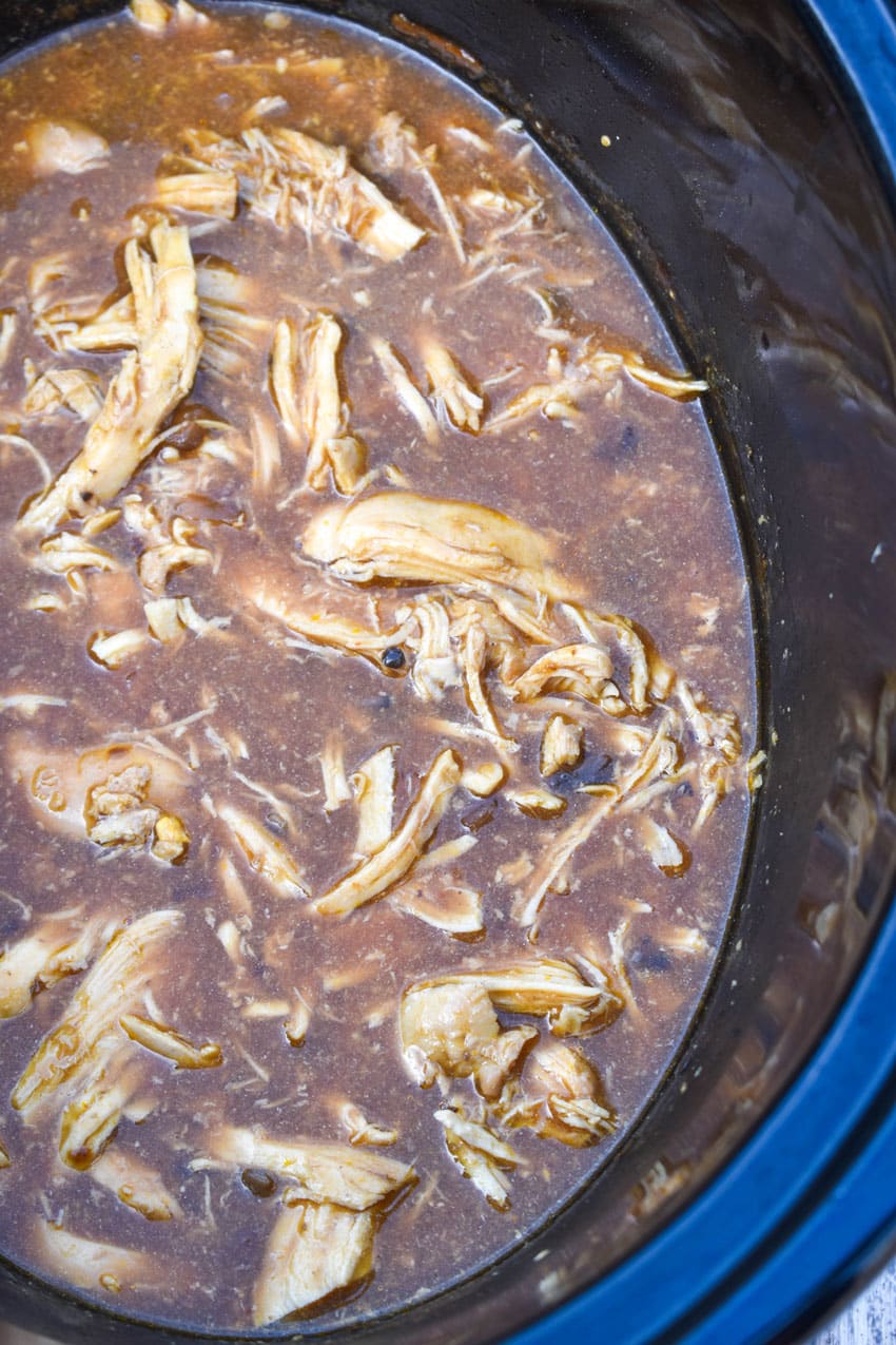 shredded chicken in brown gravy in the black bowl of a slow cooker