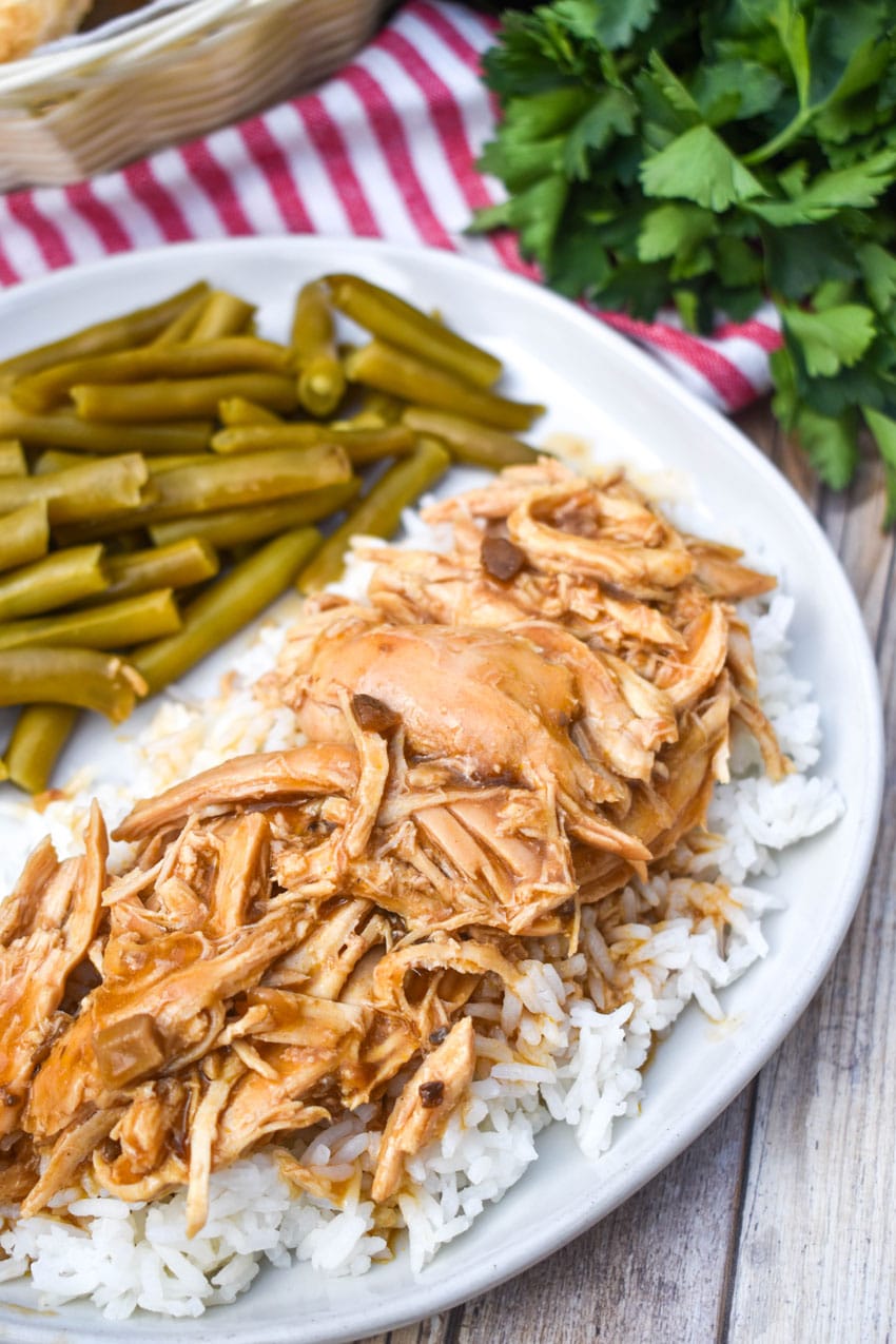 crockpot chicken and gravy over steamed white rice on a white dinner plate
