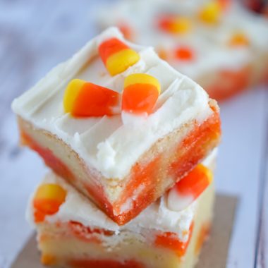 TWO PIECES OF CANDY CORN COOKIE BARS STACKED ON TOP OF EACH OTHER ON A DQUARE OF BROWN PARCHMENT PAPER