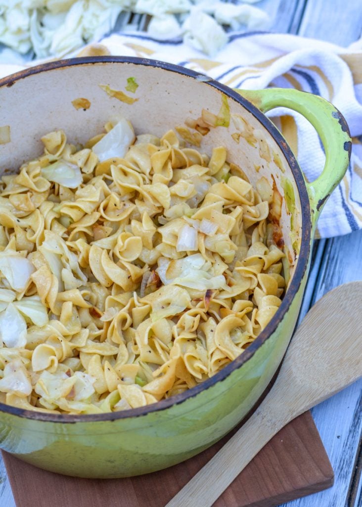 Slovakian Haluski Recipe (Polish fried cabbage & noodles) shown in an enameled cast iron dutch oven with a wooden spoon for serving