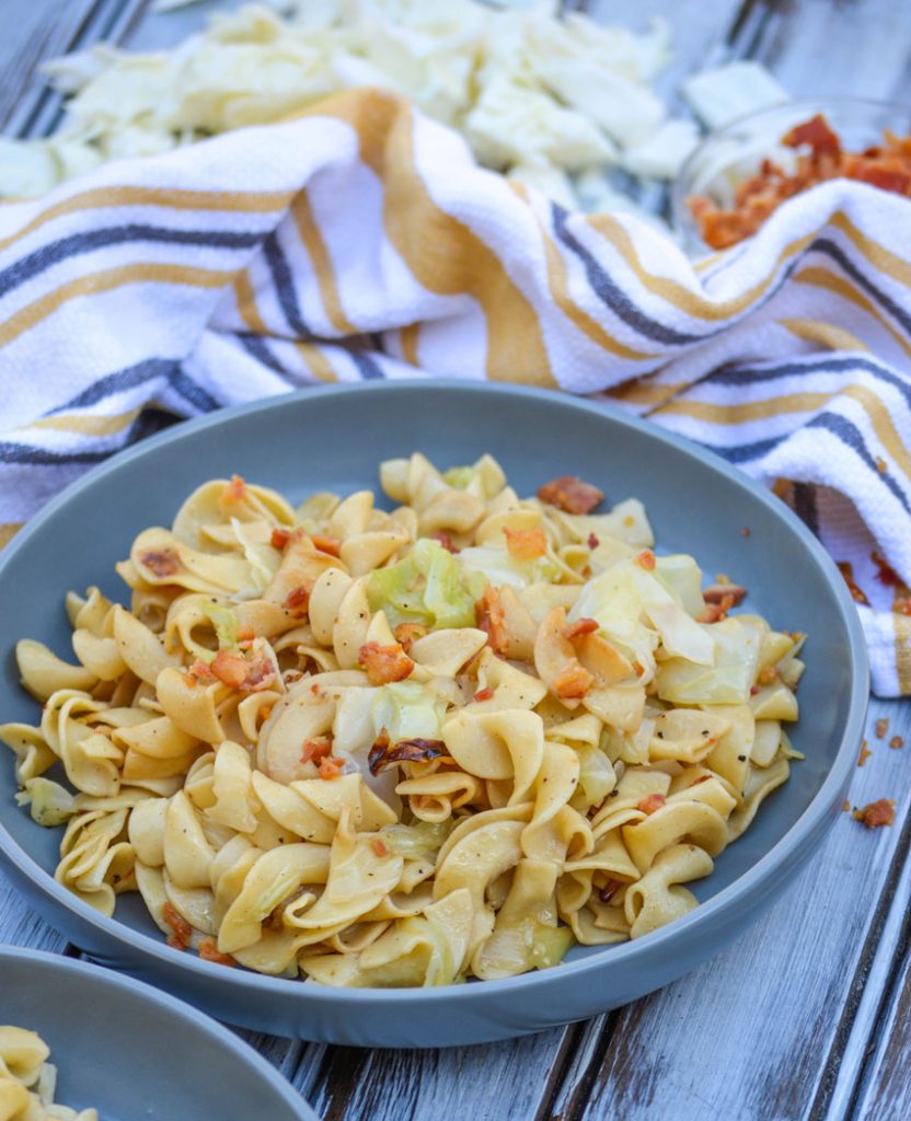 Haluski Recipe (Polish fried cabbage & noodles) topped with crisp, crumbled bacon and served on a large gray plate