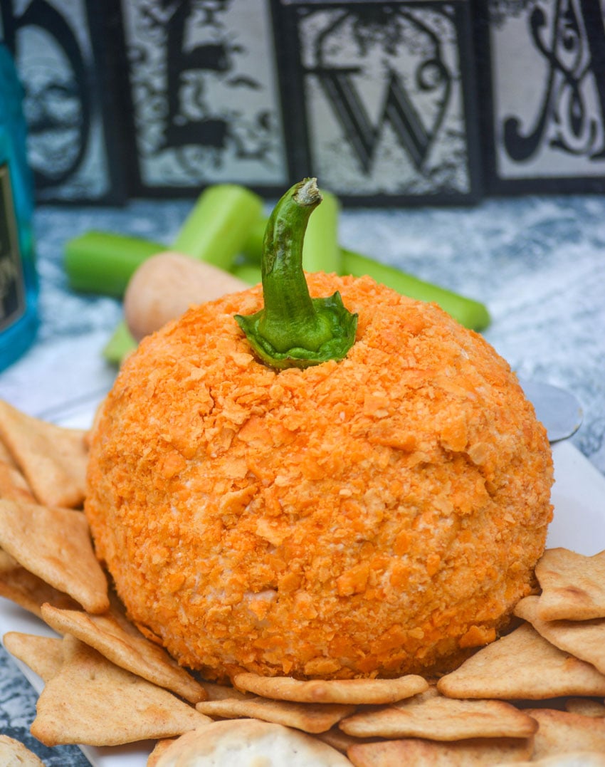 PUMPKIN SHAPED TEX MEX CHEESE BALL RESTING ON WHEAT CREACKERS ON A WHITE SERVING PLATTER