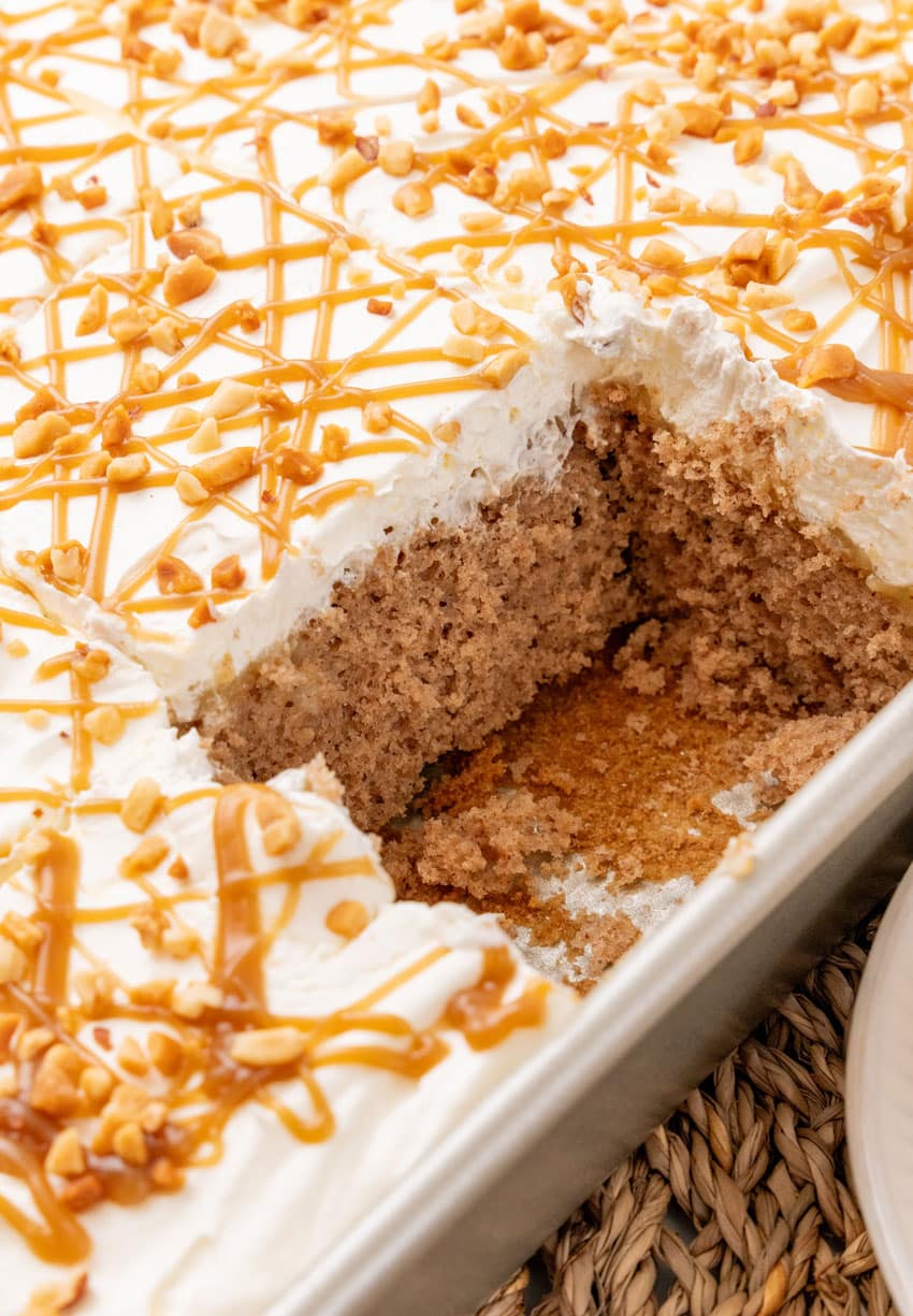 a whipped cream topped apple spice poke cake with a slice removed