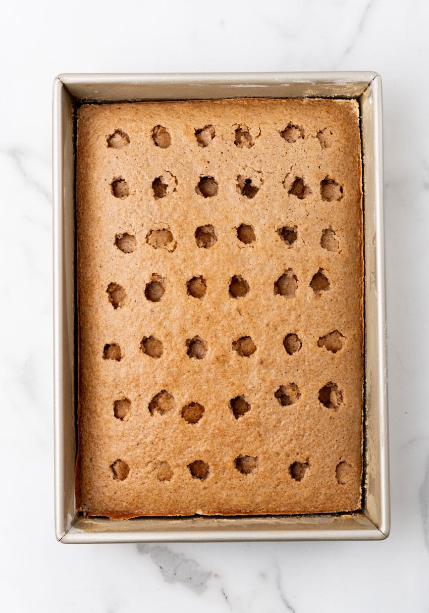 a baked spice cake with large holes poke in the top in a 9x13 inch baking pan
