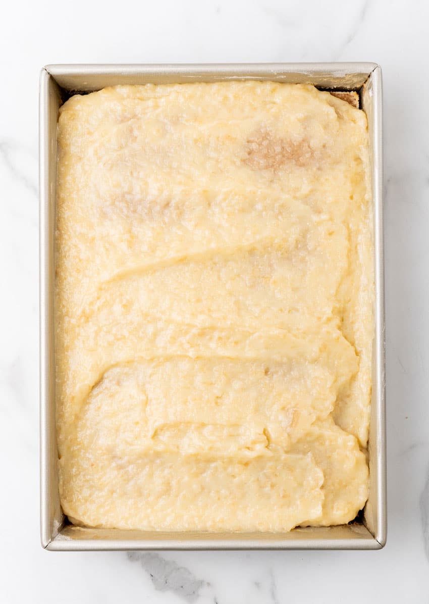 a creamy pudding and apple pie filling mixture spread overtop of a baked spice cake in a large metal baking pan