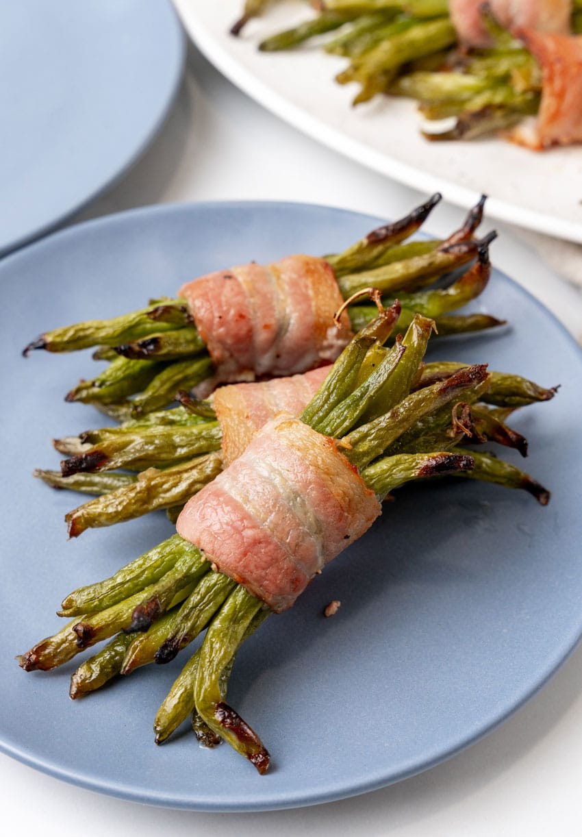 three bacon wrapped green bean bundles on a small blue plate