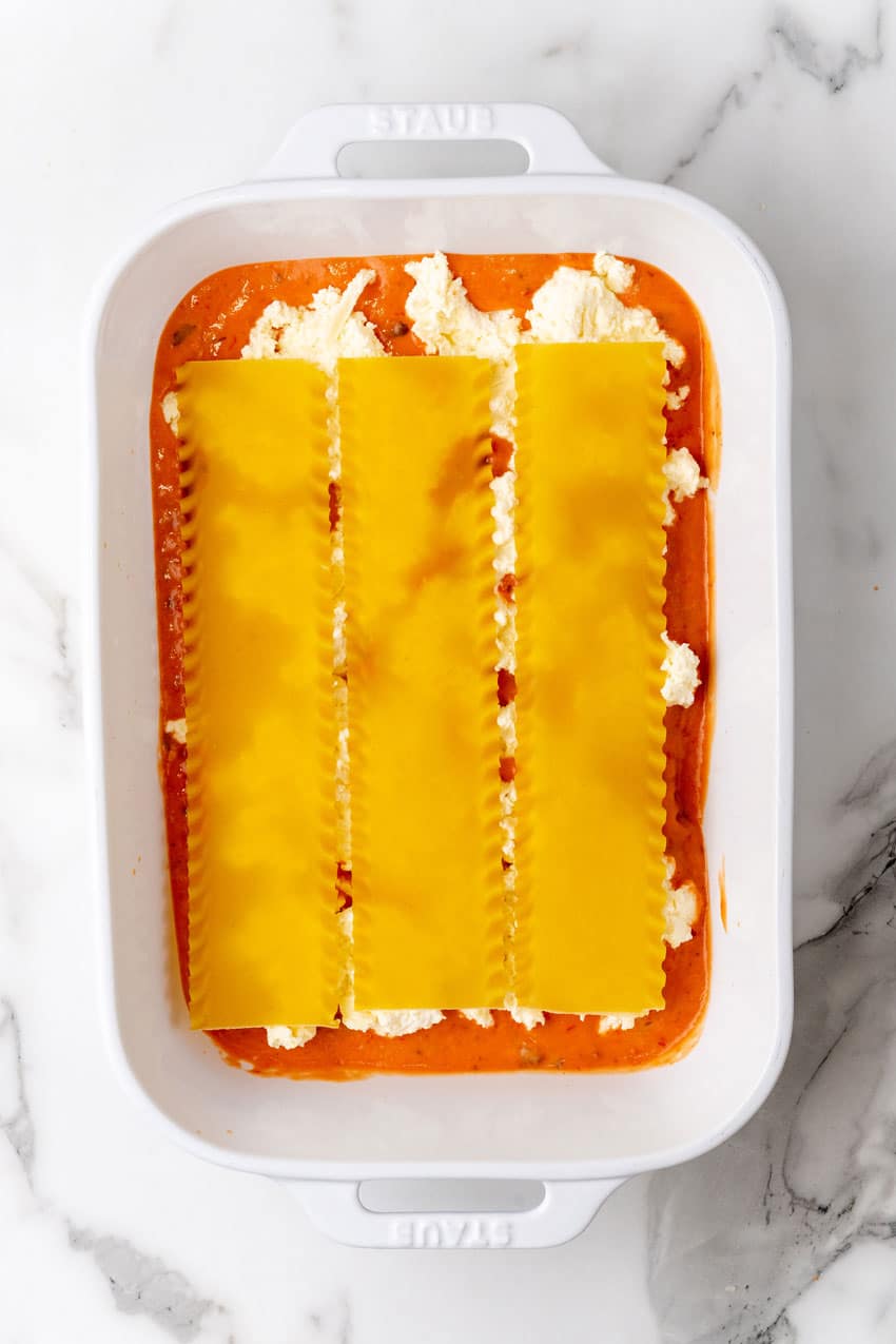 a layer of lasagna with blush sauce arranged in a white baking dish