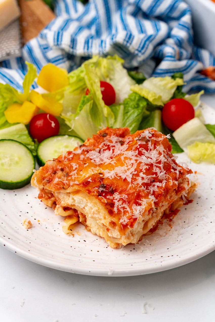 A slice of lasagna rosa on a white plate with a simple salad on the side