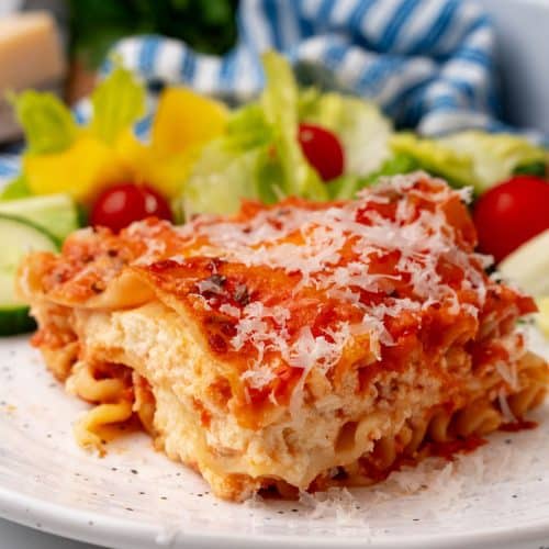 A slice of lasagna rosa on a white plate with a simple salad on the side