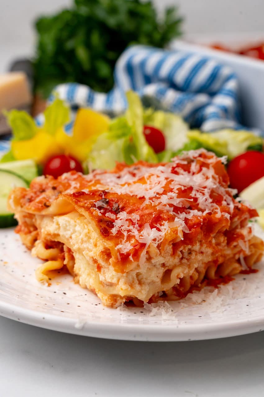 A slice of lasagna rosa on a white plate with a simple salad on the side