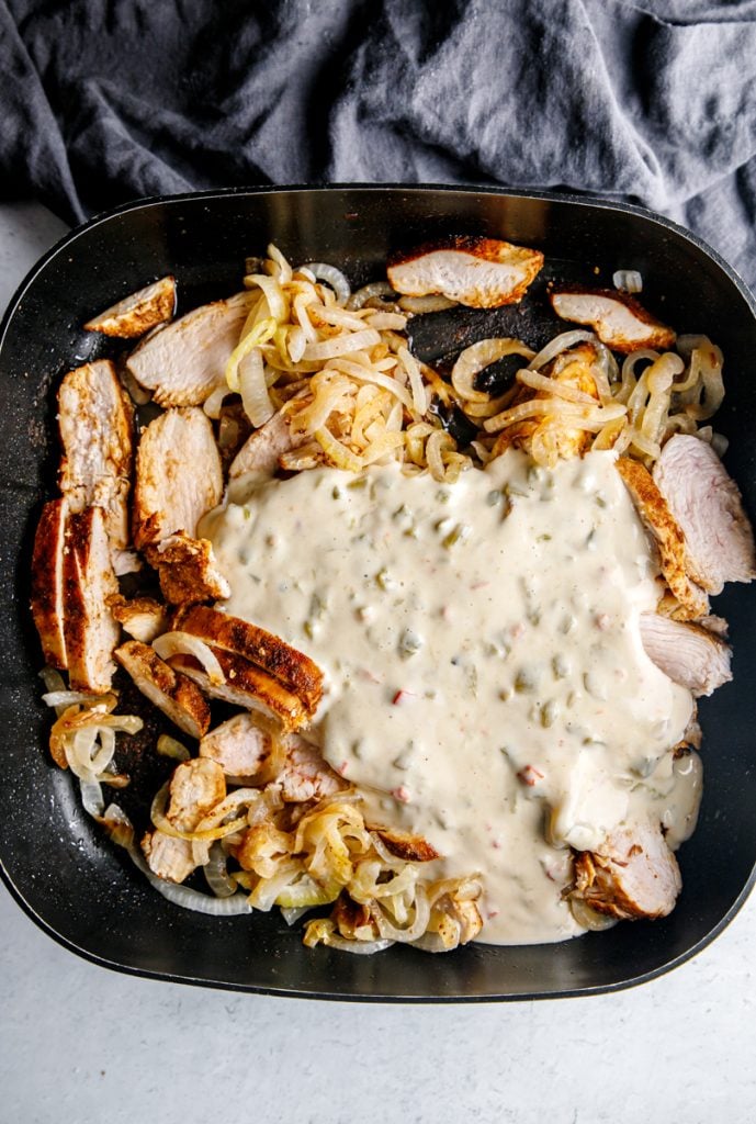queso poured over cooked chicken strips & caramelized onions in a large black skillet
