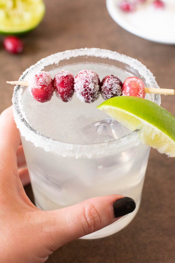 holding a glass of margarita with cranberries on top
