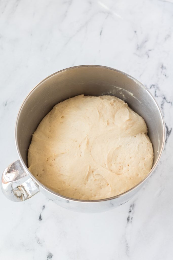 risen english muffin dough in a metal mixing bowl