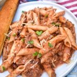 penne alla vodka with ground beef on a small white plate with a breadstick on the side