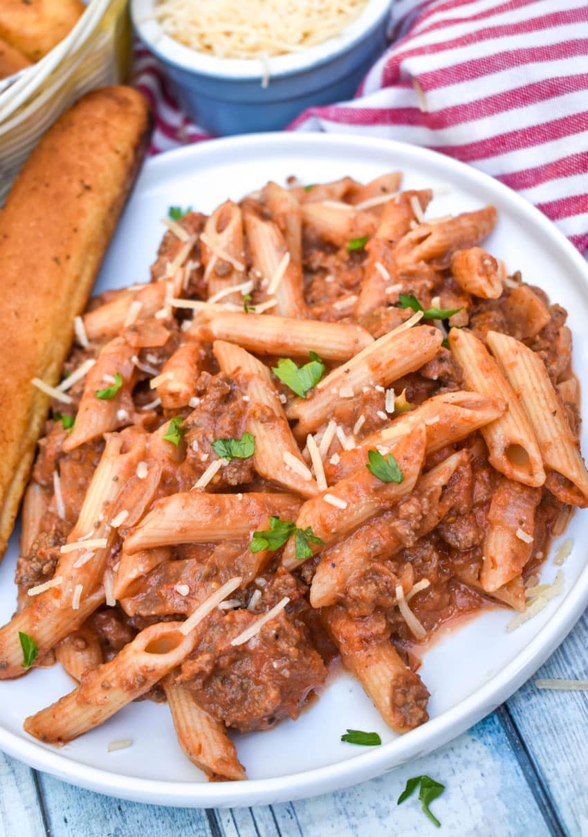 penne alla vodka with ground beef on a small white plate with a breadstick on the side