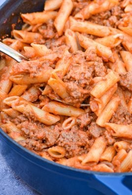 a silver spoon scooping penne alla vodka with ground beef out of a blue pot