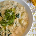 creamy chicken gnocchi pesto soup in a white bowl topped with a dollop of green pesto and shredded parmesan cheese