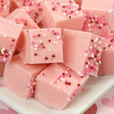 SQUARES OF PINK LEMONADE FUDGE PILED ON A WHITE SERVING PLATTER