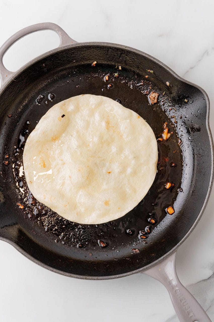 flour tortillas cooking in hamburger grease in a large black skillet