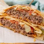 two halves of a copycat quesadilla burger stacked on a parchment paper lined wooden cutting board