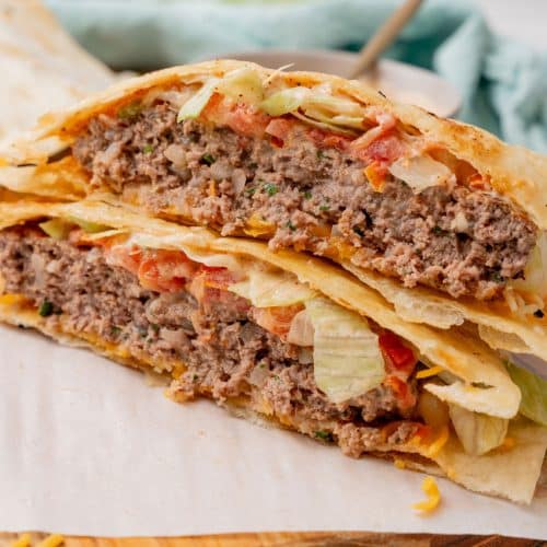 two halves of a copycat quesadilla burger stacked on a parchment paper lined wooden cutting board
