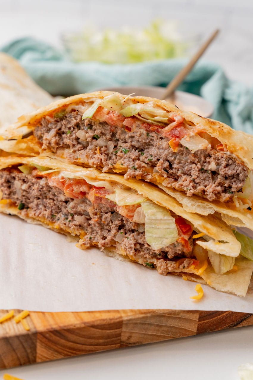 two halves of a copycat quesadilla burger stacked on a parchment paper lined wooden cutting board