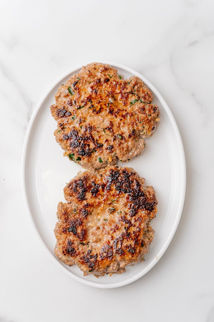 two cooked burger patties on a white serving tray