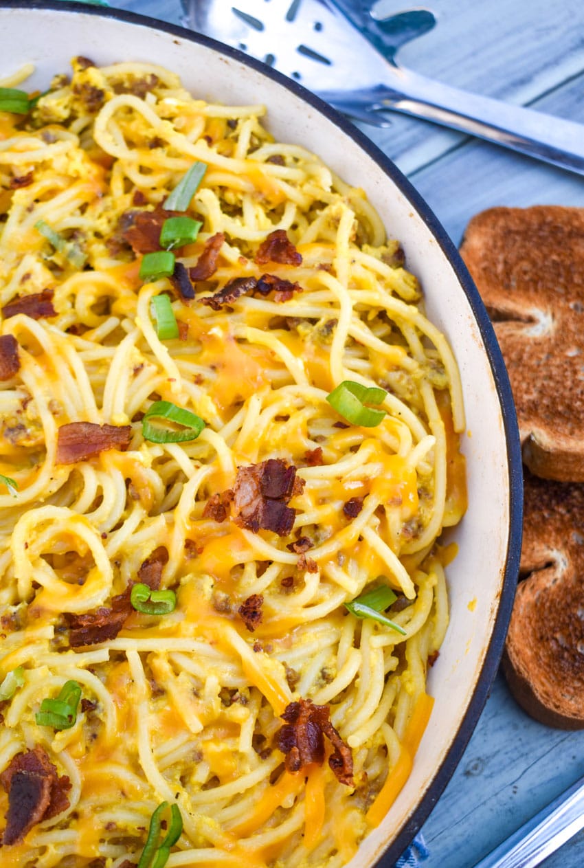 breakfast spaghetti in an enameled cast iron skillet with slices of toast on the side
