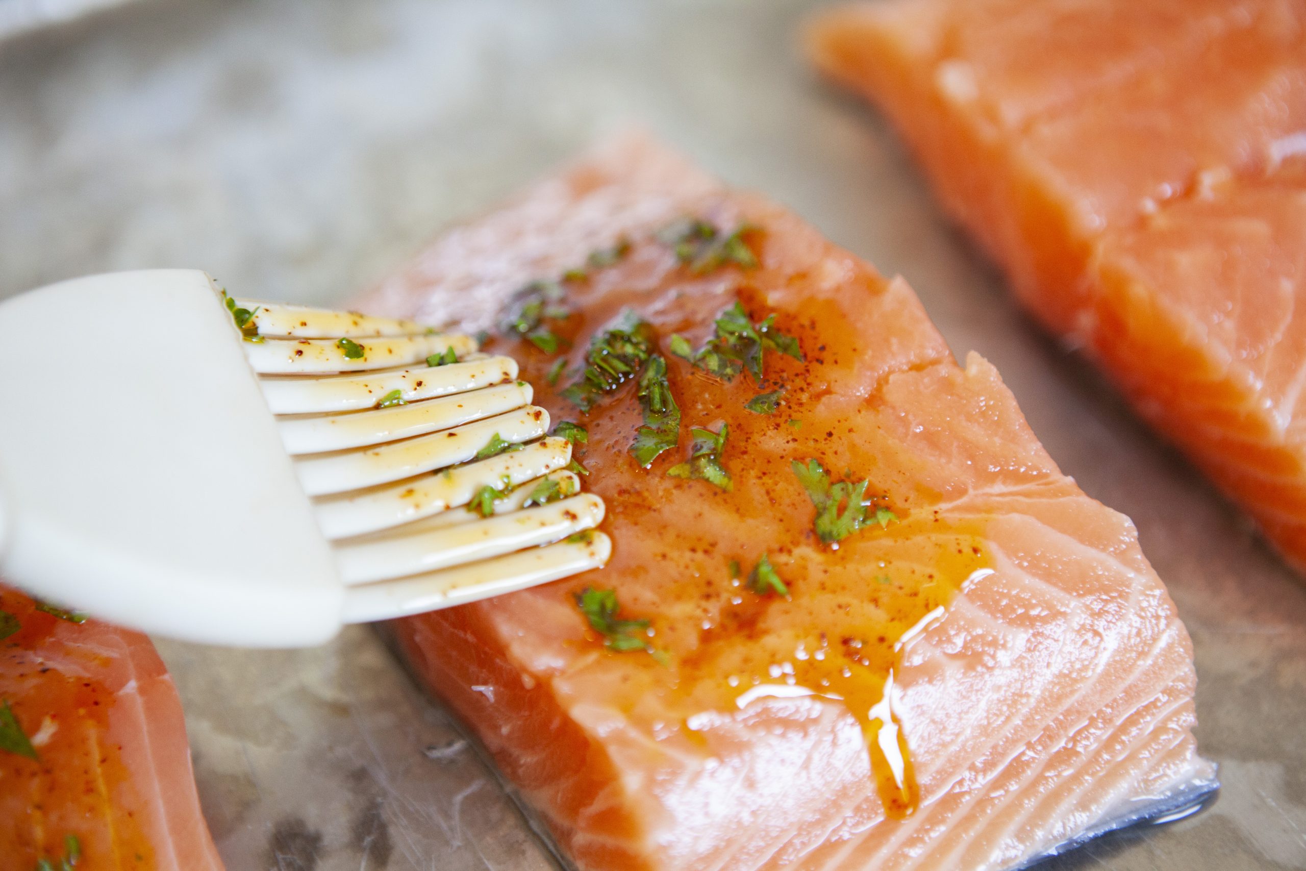 a silicone brush basting citrus marinade over raw salmon filets on a baking sheet