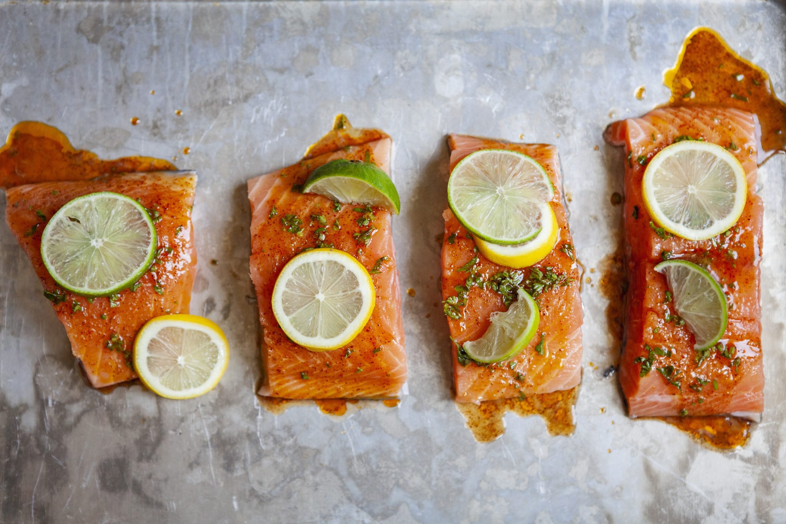 uncooked citrus marinated salmon filets topped with slices of lemon and lime on a metal baking sheet