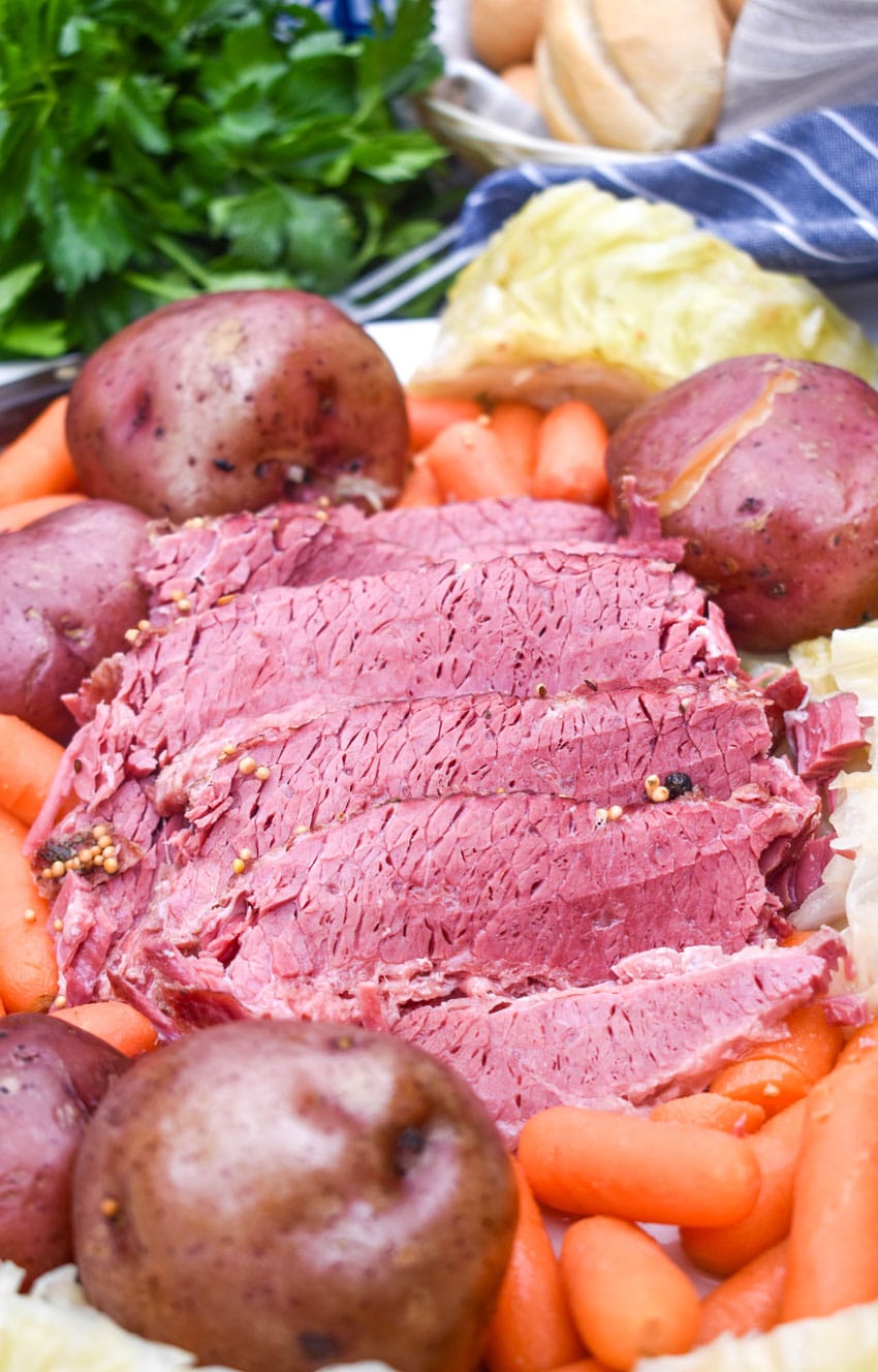 slices of cooked corned beef brisket on a white platter surrounded by potatoes cabbage and carrots