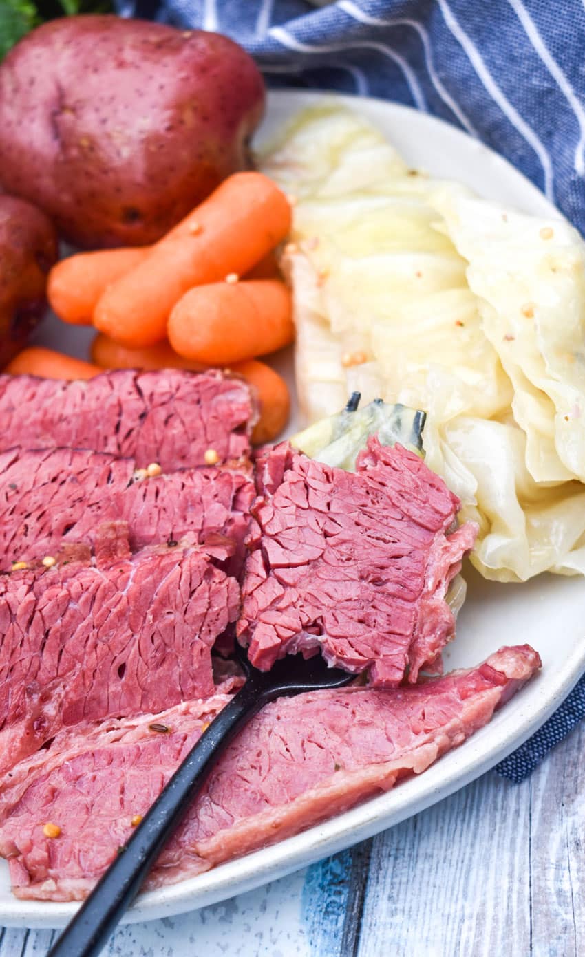 slices of corned beef brisket with red potatoes carrots and cabbage on a white dinner plate