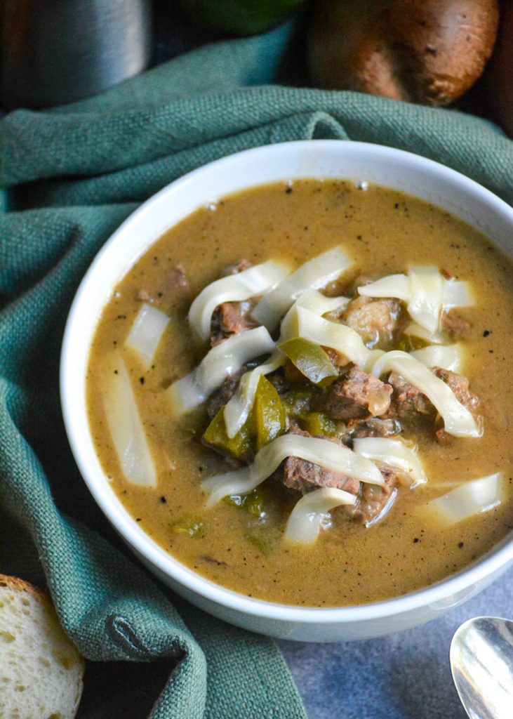 philly cheesesteak soup in a white bowl topped with melted strips of provolone cheese