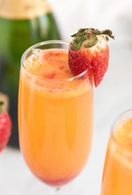 STRAWBERRY MIMOSAS IN FLUTED GLASSES WITH A SLICED STRAWBERRY ON THE SIDE FOR GARNISH