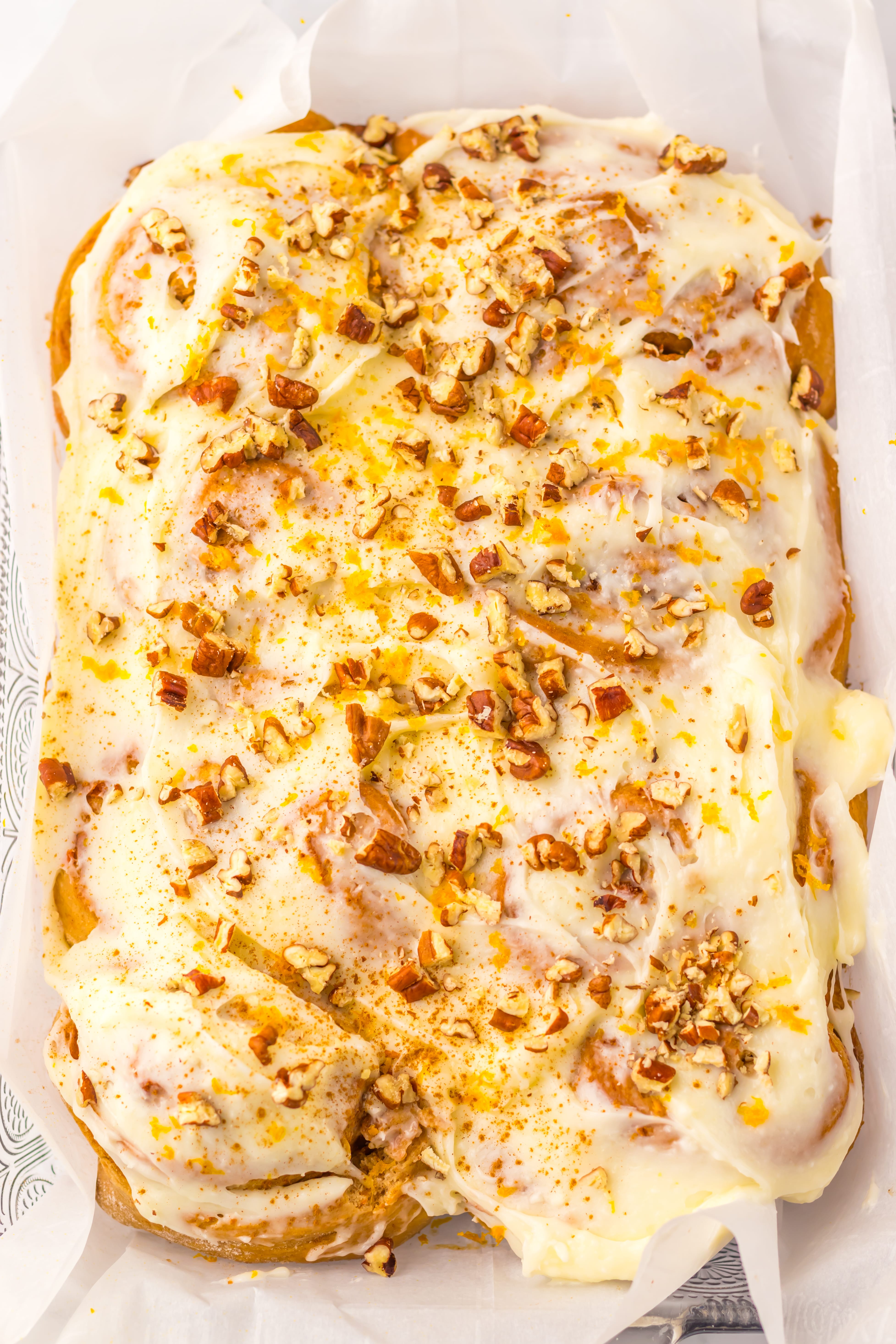 frosted carrot cake cinnamon rolls in a parchment paper lined glass baking dish