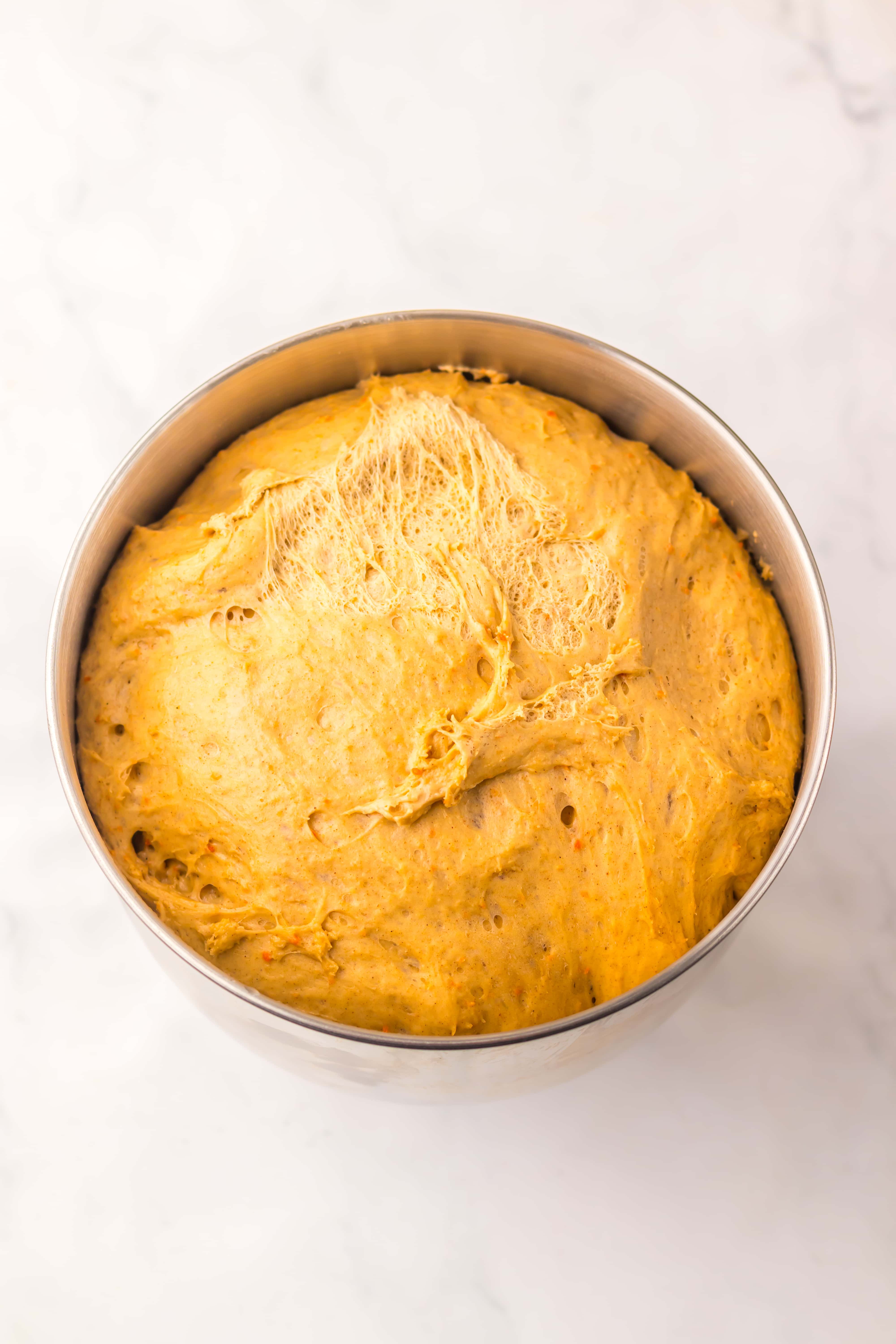 risen carrot cake cinnamon roll dough in a metal mixing bowl