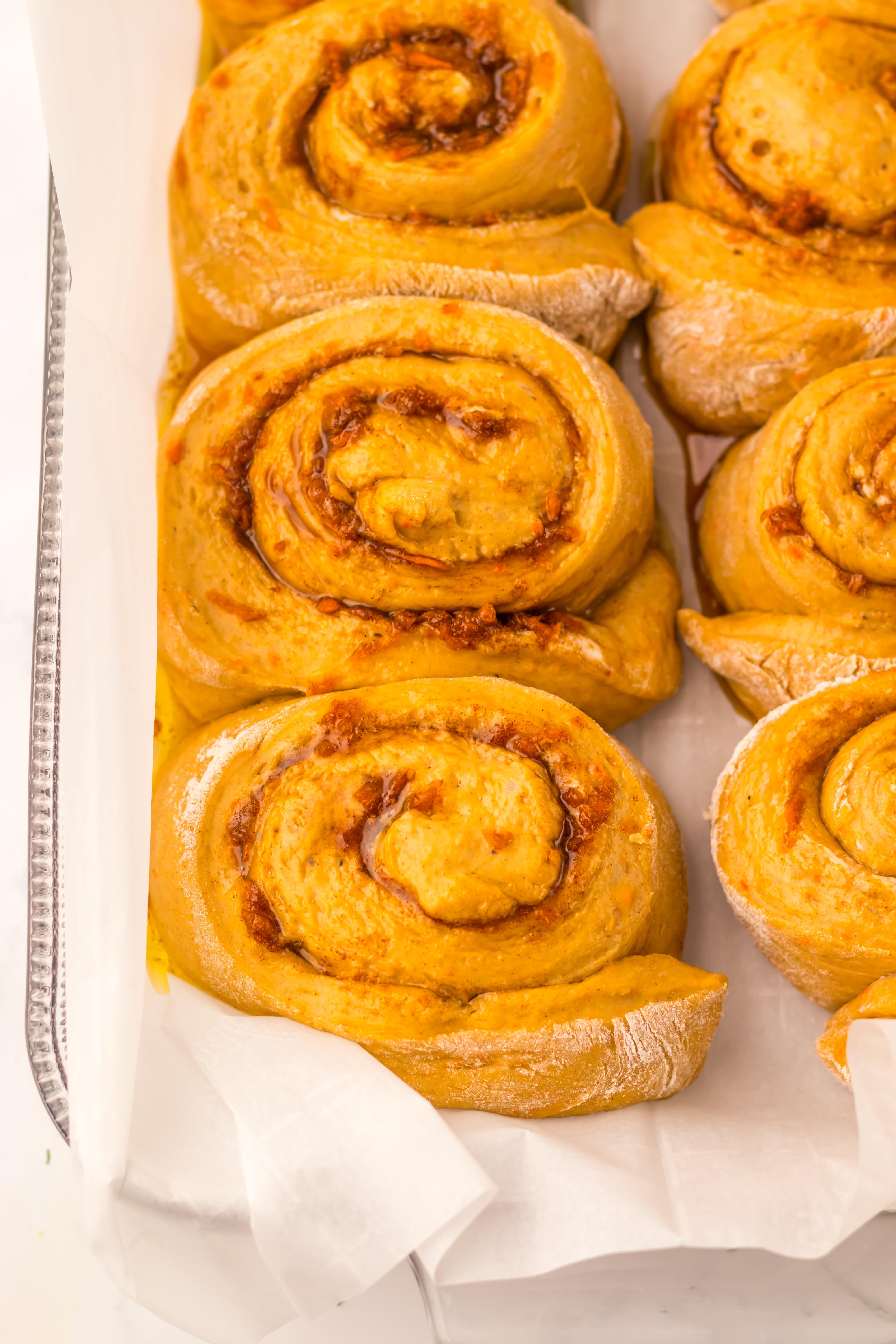 unbaked rolled carrots cake cinnamon rolls in a parchment paper lined glass baking dish