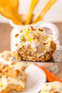 a metal spatula holding up a homemade frosted carrot cake cinnamon roll