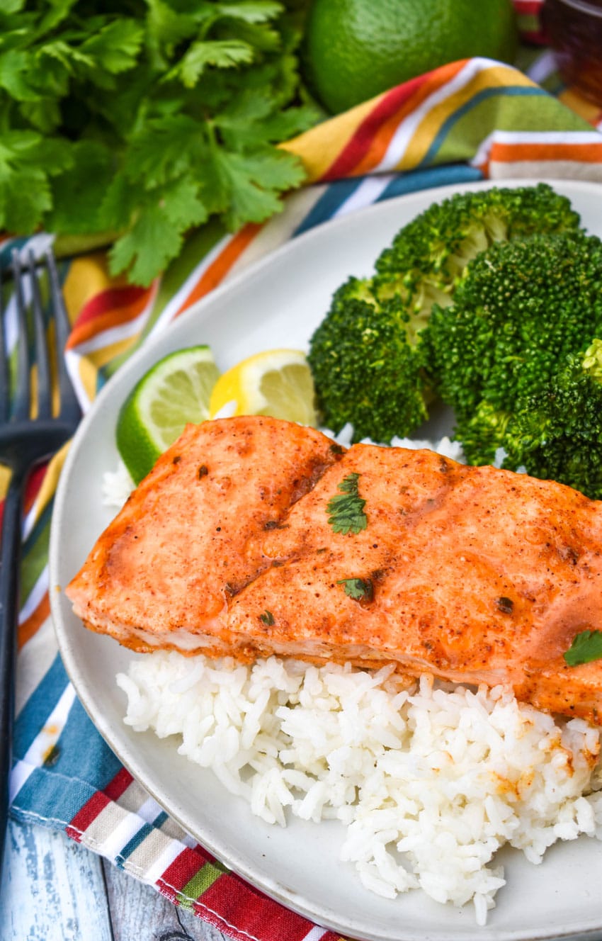 a slice of citrus salmon on a bed of steamed white rice on a white plate with steamed broccoli on the side