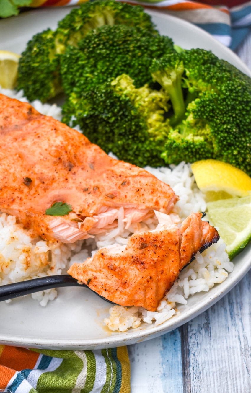a slice of citrus salmon on a bed of steamed white rice on a white plate with steamed broccoli on the side