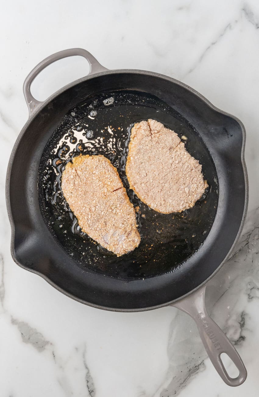 two pieces of homemade pork schnitzel frying in a black skillet