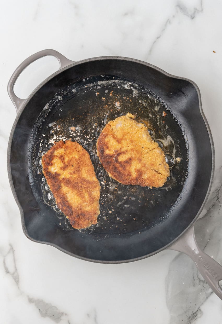 two pieces of homemade pork schnitzel frying in a black skillet