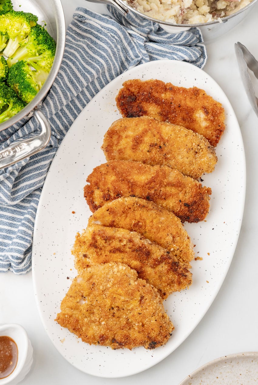 pieces of homemade pork schnitzel arranged in a row on a white serving platter