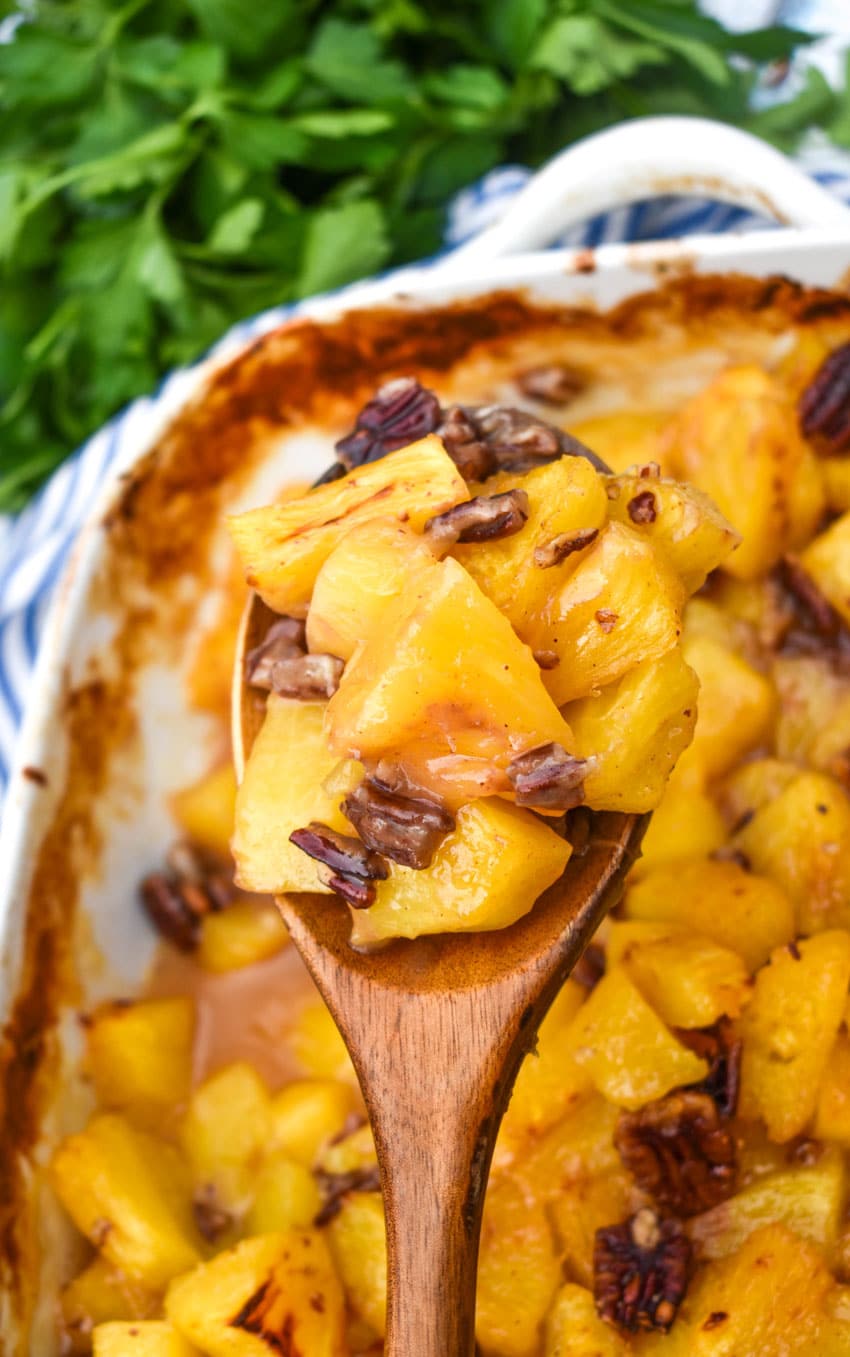 a wooden spoon holding up a scoop of brown sugar roasted pineapples