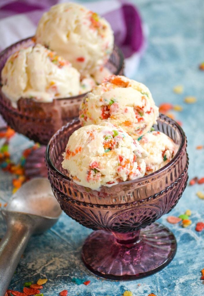 scoops of fruity pebble ice cream shown in two purple glass bowls on blue background