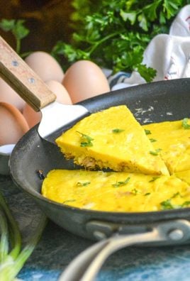A WOODEN SPATULA LIFTING A SLICE OF TUNA FRITTATA OUT OF A LARGE BLACK SKILLET