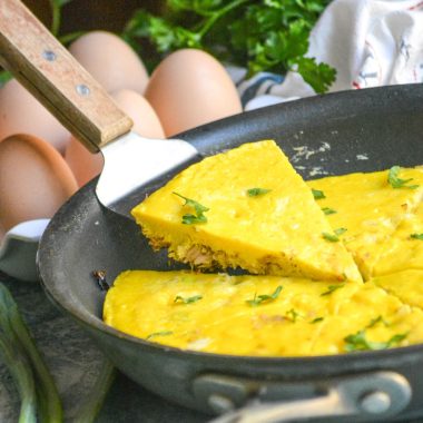 A WOODEN SPATULA LIFTING A SLICE OF TUNA FRITTATA OUT OF A LARGE BLACK SKILLET