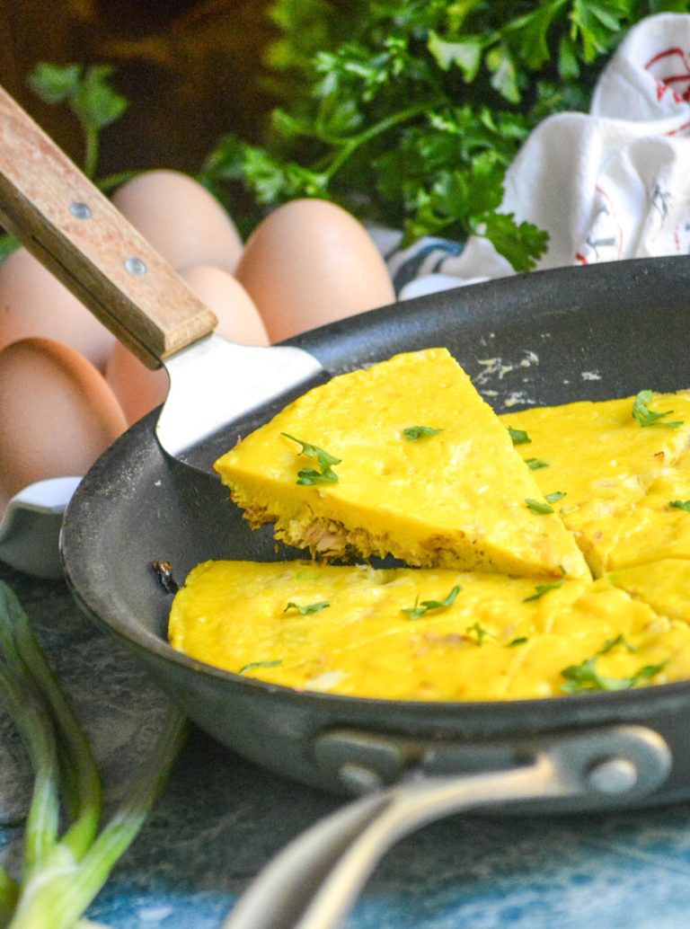 A WOODEN SPATULA LIFTING A SLICE OF TUNA FRITTATA OUT OF A LARGE BLACK SKILLET