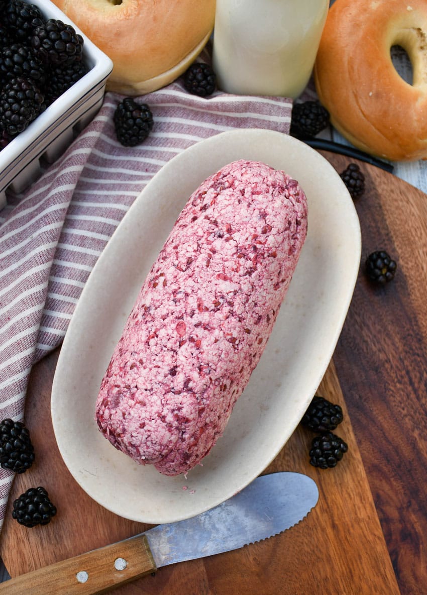 a log of whipped blackberry butter on a small dish on a wooden cutting board